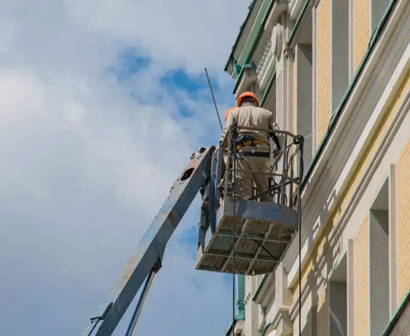 Artisan casqué sur une nacelle lors d’une intervention sur la façade claire d’un immeuble.