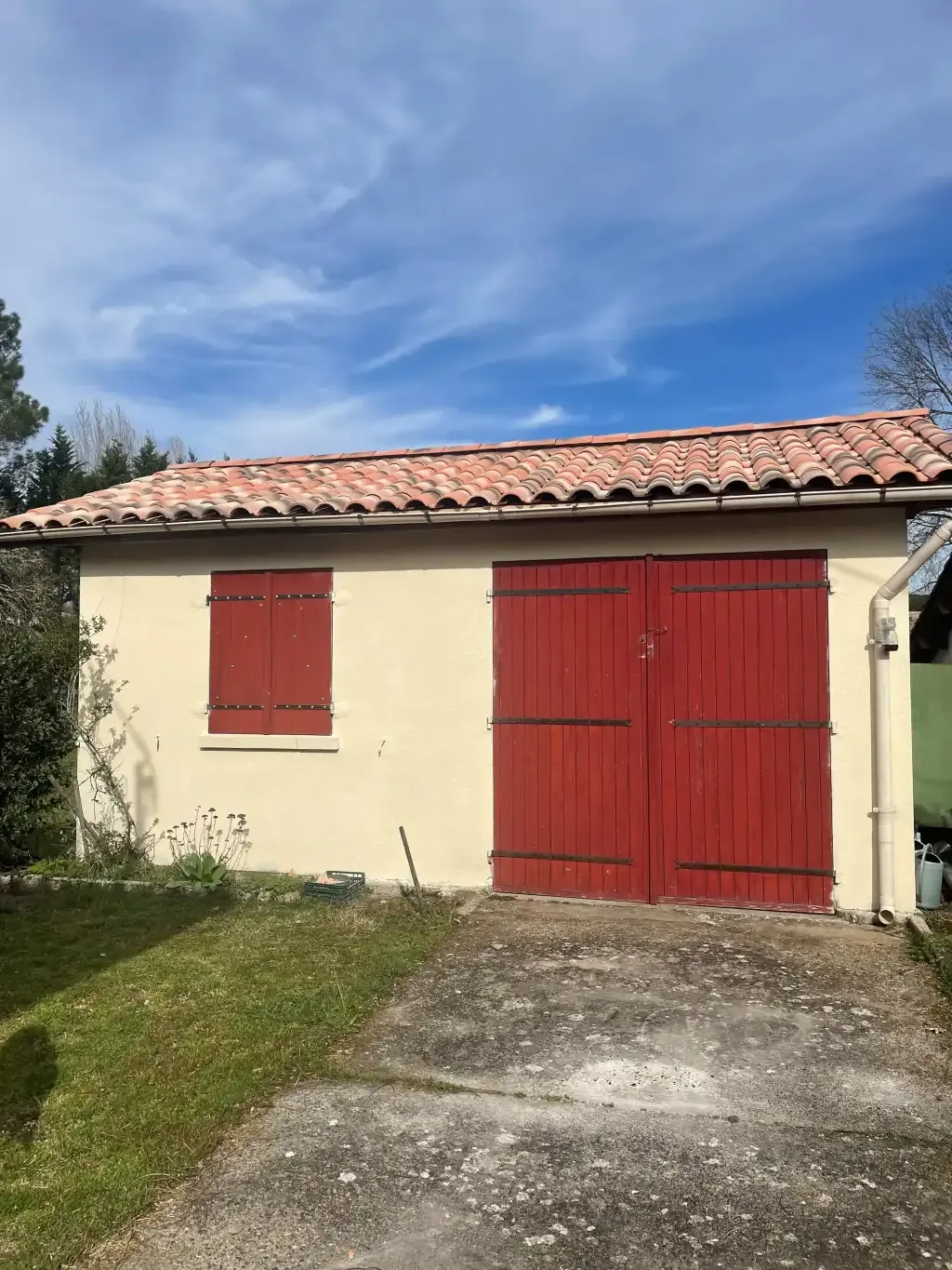 Garage à façade crème avec volets rouges et toiture en tuiles canal.