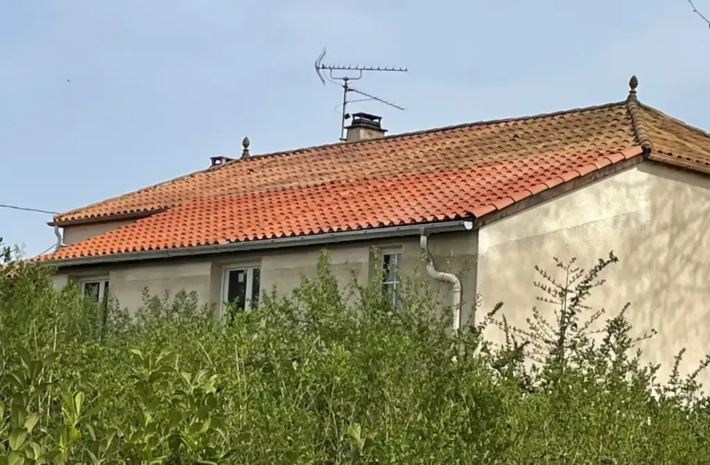 Maison aux murs clairs avec toiture en tuiles rouges, gouttières et cheminées.